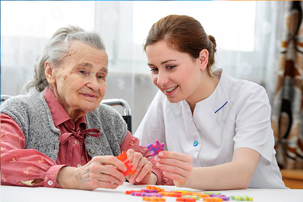 Female home caregiver talking with senior woman, sitting in living room and listening to her carefully.